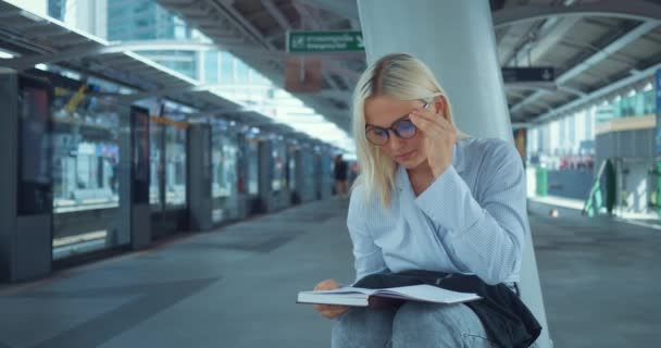 在地铁站读书的女人 布朗德教育成功的年轻女子在户外看书 城市城市街道地铁站的白人妇女 城市生活概念 — 图库视频影像