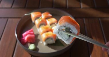 Çubuklarda suşi, yakın çekim. Geleneksel Japon Asya mutfağı. Suşi Philadelphia rulolarını ayarladı. Öğle yemeği, akşam yemeği, suşi barda kahvaltı, restoran, kafe. Parlak sabah güneşi leziz yemekleri aydınlatıyor.
