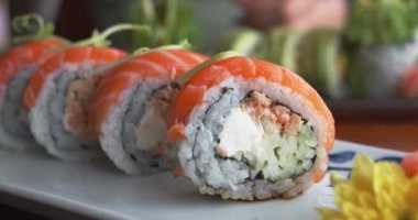 Suşi seti, tabakta Asya yemeği. Geleneksel Japon yemekleri. Yeşilliklerle süslenmiş suşi, beyaz tabakta servis edilen taze pişmiş suşi ruloları. Restorandaki suşi barında sergilenen sanat eseri.