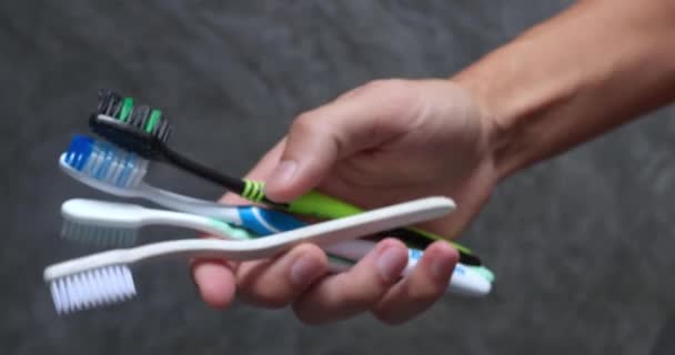 用男性的手刷牙 在灰色浴室的背景下拿着彩色牙刷的男人 各式正位正确的右牙刷 以正确刷牙 口腔保健概念 — 图库视频影像
