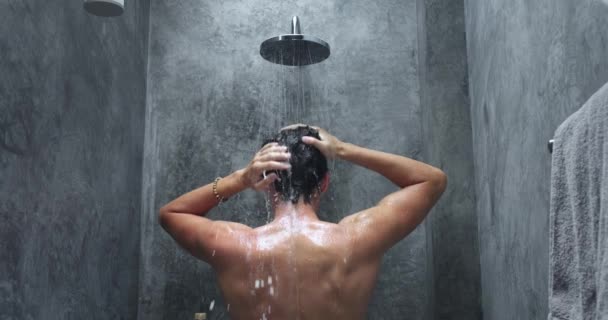 シャワーバックビューで洗濯する男 男はシャワー 灰色のバスルームで頭と体を洗っています 仕事の前の朝のプロシージャ 洗浄の泡立つクリーニング バックビュー リアビュー — ストック動画