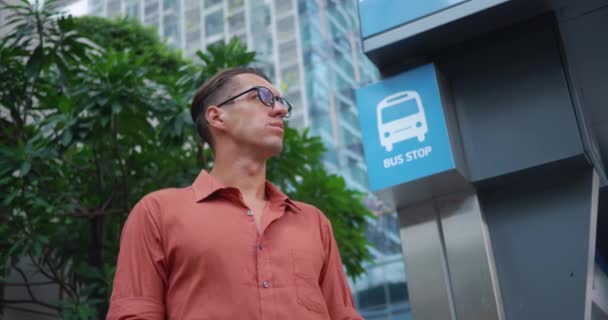 男子眼镜等待公共汽车旅行 预计每天的公共汽车旅行 个人旅行 公共交通 — 图库视频影像