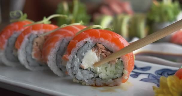 箸でレストランで寿司を食べる 近づいて 箸は赤い寿司ロールをつかみ 醤油に浸して食べて楽しむ 緑に包まれた美しい味わいのお寿司 — ストック動画