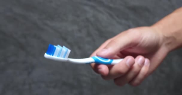 男性手拿着牙刷 男人举手 旋动蓝白的牙刷 矫正牙刷 清洁假牙 牙冠和牙套 去除菌斑的概念 灰色浴室墙壁背景 — 图库视频影像
