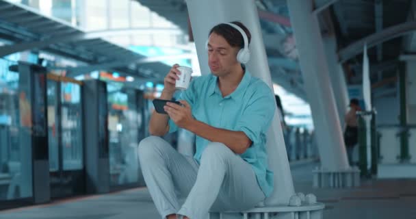 Homem Senta Nos Auscultadores Estação Olha Para Telefone Põe Copo — Vídeo de Stock