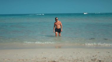 Denizden çıkan adam yan bakar. Denize bakan adam, deniz keyfine doğru bakar. Sahil tatili, vücuda uygundur. Suda duran adam deniz kenarının cazibesini temsil eder. Sahilde yaşamanın huzurunu bozar.