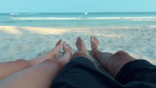 第一眼看到的是情侣们的腿在沙滩上休息 看着大海 沉浸在欢乐的放松中 温暖的沙滩抚摩着她们的腿 她们沐浴在热带天堂的宁静氛围中 — 图库视频影像