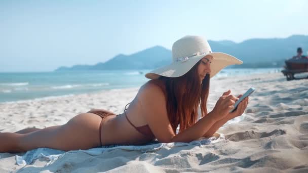 Женщина Бикини Женщина Шляпе Лежит Пляже Помощью Телефона Пляжный Отдых — стоковое видео