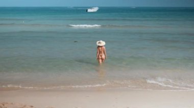 Bikinili ve şapkalı bir kadın okyanusa doğru yürür. Işıl ışıl güneşin tadını çıkarır. Dalgaların hafif dokunuşları. Kadın okyanusların derinliklerine doğru yürür. Gök mavisi, okyanusta teselli arayan deniz manzarasının dinginliği içinde eğlenir.