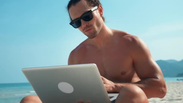Uomo Occhiali Sole Nomade Digitale Seduto Sulla Spiaggia Che Lavora — Video Stock