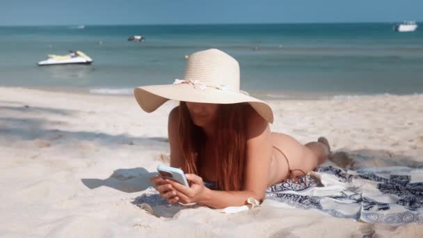 Женщина Шляпе Бикини Лежит Песчаном Пляже Используя Мобильный Телефон Отпуск — стоковое видео