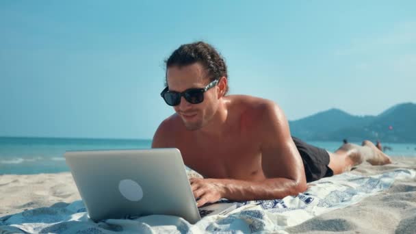 Mann Mit Sonnenbrille Liegt Strand Und Tippt Auf Laptop Inmitten — Stockvideo