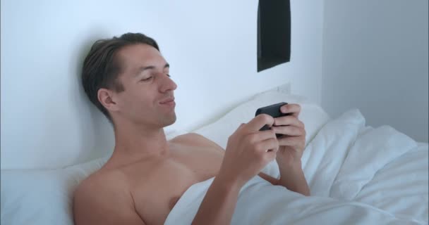 Ειρηνικός Πρωινός Άντρας Ξαπλωμένος Στο Κρεβάτι Ελέγχει Τηλέφωνο Συγχρονίζεται Τον — Αρχείο Βίντεο