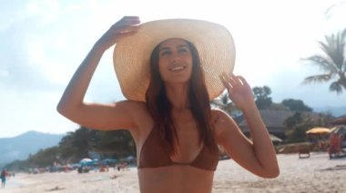 Bikinili ve büyük hasır şapkalı çekici bir kadın yaz tatilinde dinlenmekten hoşlanıyor. Dişi, güneş ışınlarının ısınmasını sever. Kadınlar temiz deniz havası soluyan huzurlu bir sahil atmosferinden hoşlanırlar.