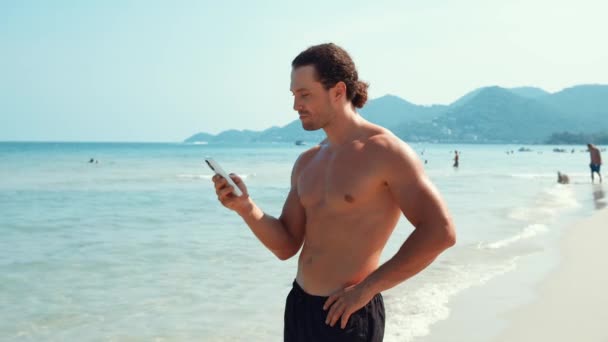 Uomo Attraente Sulla Spiaggia Comunica Con Gli Amici Telefono Trovare — Video Stock