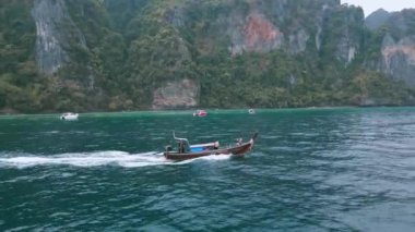 Krabi, Tayland, 23 Aralık 2023. Geleneksel Tayland gemisi görkemli kayalarla çevrili olarak denizde yüzüyor. Tekne, doğal güzellikler arasında suda hızla süzülür. Tekne kayaların arasından okyanusta geçiyor.