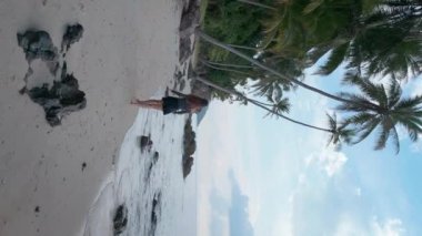 Uzun saçlı ince kız kumlu sahil ruhuyla seyahat ediyor. Dalgalanan okyanus ve tropikal palmiyelerin yanında güzel bir seyahat sahnesi. Özgürlük, macera ve seyahat güzel bir şekilde birleşir. Dikey video