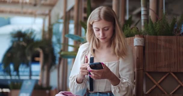 Blondynka Dziewczyna Letnie Ubrania Stoi Tropikalna Kawiarnia Przewijając Przez Telefon — Wideo stockowe