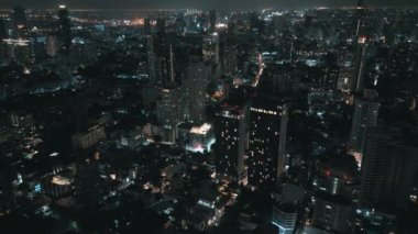 Gece vakti sinematik metropol şehri. Şehir merkezi sokakları şehir ışıklarıyla aydınlatılmış. Gece şehri insansız hava aracı tarafından ele geçirildi. Modern metropolün binalarıyla dolu gece şehrinin havadan görünüşü.