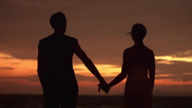 Aşık siluet çift. Erkek, altın gün batımının arka planında bir dişiyi elinden tutar. Günbatımında birbirine aşık romantik bir çift akşam denizin arka planına karşı. Romantik randevu kavramı.
