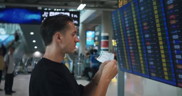 男性旅行者は 空港の飛行機のスケジュール出発を見るチケットを保持しています フライトインフォメーションボードでコーカサス人の旅行者 フライトをチェック 旅行コンセプト バンコク Sep 2023 — ストック動画