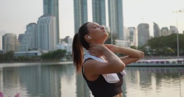Parkta dinlenen ve kulaklıkla müzik çalan bir kadın. Kulaklıkla şarkı dinleyen arkadaki şehir silueti huzur ve gençleşme anlarında şehir müziği senfonisi coşuyor.