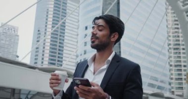 İş adamı takım elbiseli adam cep telefonu dengeleme ve hareket kabiliyeti kullanarak bir fincan kahve içiyor. İş elbisesi giymiş bir adam, sofistike bir amaç için kahve içip akıllı telefon yazıyor.