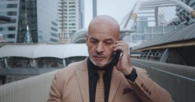 İş adamı, şehir hayatında akıllı telefon işiyle ilgili görüşmeler yapıyor. Akıllı telefon görüşmeleri yapan bir işadamı, şehir sokaklarında akıllı telefon konuşmalarıyla dolaşırken modern iş ortamını şekillendiren kararlar alır.