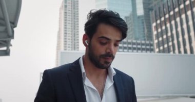 Takım elbiseli ve kulaklıklı bir adam şehir caddesinde yavaşça yürüyor. Kablosuz kulaklıklar modern cihazlara olan tutkuyu gösteriyor. Adam şehir ritmine konsantre olmak için kulaklık ya da podcast dinliyor.