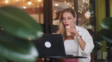 Yemyeşil bitkileri olan güzel bir kafe. Serbest çalışan beyaz kadın bilgisayarlı uzaktan kumanda üzerinde çalışıyor. Göz kamaştırıcı kafeterya yemyeşil bitkiler serbest çalışan yetişkin kadın bilgisayar uzaktan kumandası üzerinde çalışıyor.