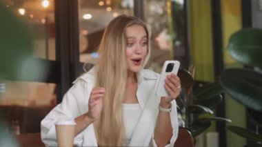 Sarışın kadın gülümsemesi, akıllı telefon yüz ifadesine, olumlu duygulara, başarıya ve mutluluğa sevinçle bakar. Yüzünde tebessüm olan sarışın kadın akıllı telefon başarısı hissine bakar.