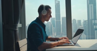 Konforlu ofis çalışanı dizüstü bilgisayarda müzik kulaklığı dinliyor serbest çalışan. Milenyum erkeği, evde çalışan ve her hareketinde klavye bilgisayarında yazı yazan müzikten hoşlanır.