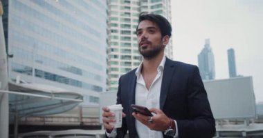 Takım elbiseli adam şehirde bir fincan kahve, akıllı telefon özgüveni ve yeterliliğiyle dolaşıyor. İş adamı takım elbiseli biri cep telefonu şirketlerinin dünyasında profesyonelce dolaşıyor.