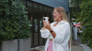 Göz kamaştırıcı kadın, telefonun yüzüne bakıyor. Kollarına gerçek bir sevinç, başarı ve olumlu duygular yayıyor. Sarışın kadın, gerçek mutluluk ve başarı dolu kadın güzelliğiyle telefona bakıyor.