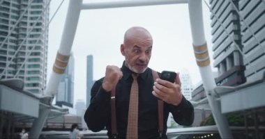 İşadamı iş yerindeki akıllı telefonlara mutlu bir şekilde bakıyor. Geniş gülümseme, başarılı anlaşmanın sevincini gösteren yüzü aydınlatır. Jestler ve yüz ifadeleri samimi bir neşe ifade eder