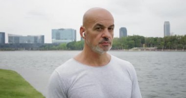 Kablosuz kulaklıklı ciddi bir adam şehir parkındaki göllere düşünceli bir şekilde bakıyor. Doğayı sarmak derin düşüncelere ilham verir, adamım. İnsan güzellik doğası ile birlik içinde sorunlara ilham ve çözüm arar.