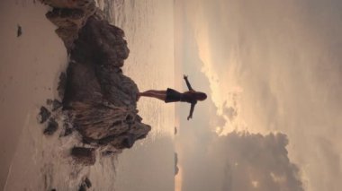 Kız, arka kamera, plaj taşları, gün batımını kucaklayan kollar. Doğanın görkemli oyunu. Doğa tarafından kucaklanan siluet, günbatımı dans ışık gölgesini birleştirir. Doğa kucaklıyor, birlik olma güzelliği. Dikey video