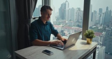 Serbest çalışan yetişkin Kafkas işçisi dizüstü bilgisayar panoramik pencerelerde çalışıyor şehir manzarası, modern mimari metropol milenyum erkek laptopçu serbest ofis ile çalışıyor