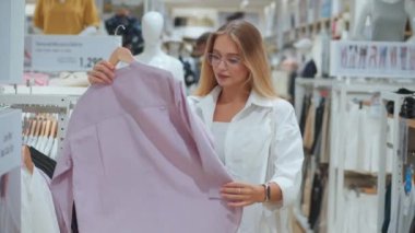 Kadın giyim mağazasındaki genç kadın yeni alışverişler için yeni kıyafetler seçiyor. Kadın giyim mağazasında yeni kıyafetler seçen, yeni alışverişler düşünen bin yıllık bir kadın.