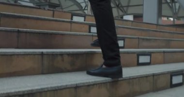 İş pantolonu içinde insan bacakları ve şehir merkezinde güçlü adımlarla yürüyen ayakkabılar. Aceleci adımlar, adımlar boyunca ritmi açıkça yener. Tek tek kasıtlı olarak geride bırakılan adımlar.