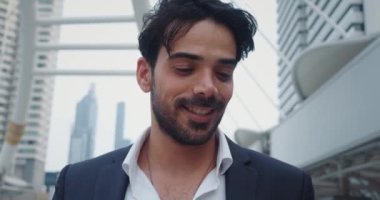 Orta Metropolis Caddesi 'nde takım elbiseli, gülümseyen Orta Doğulu iş adamı. İşadamı aşağı bakar ve etrafındaki gökdelenleri inceler. Gülümseme başarılı bir iş adamı izlenimi yaratır