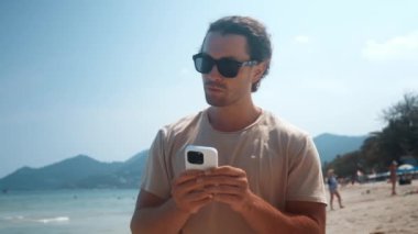 Millennial güneş gözlüklü kumsal boyunca yürür, telefona bakar ve mesajlaşır. Cennetteki dış dünyayla cep telefonu bağlantısı. İnsan tropik adanın tadını çıkarırken telefon yazıyor.