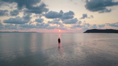 Günbatımında deniz kıyısında duran insan bulutlu gökyüzüne karşı doğanın sakin günbatımı resimli gökyüzüne karşı. İnsanoğlu karanlık çökünce okyanusun kıyısında durur. Bulutlar tepemizde sersemletir. Huzurlu günbatımı ve manzaralı gökyüzü.