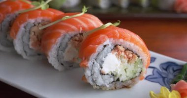 Lokanta masasında suşiye odaklanmış enfes tabaklar. Restoran masasında suşi rulolarını yakından gören Japon mutfağı dünyası. Suşi rulosu beyaz tabakta.. 