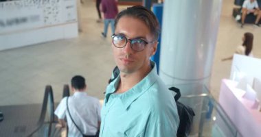 Adam yürüyen merdivenden iniyor, arkasına bakıyor. Şehir çevresi. Yürüyen merdiven ortamı. Arka plan sahneyi büyütüyor. Erkek yolculuğu. Şehir merkezi, özünde şehir hayatı yürüyen merdiven alçalıyor.