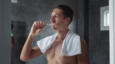 Milenyum insanı banyoda dişlerini fırçalarken ağız hijyeni diş fırçalarken. Beyaz erkek, banyoda durmuş diş fırçalıyor banyo atmosferinde diş temizliği yapıyor.