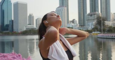 Şehir ormanındaki kadın şehir parkında duran müzik kulaklıklarını dinlerken dinleniyor. Etrafı gökdelenlerle çevrili, kulaklıkla müzik dinleyen bir kadın.