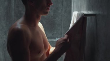 Banyodaki beyaz adam kişisel hijyen ritüelleri için havlu alıyor. Banyodaki adam havluyu alır ve banyodaki kişisel temizliğe odaklanır.