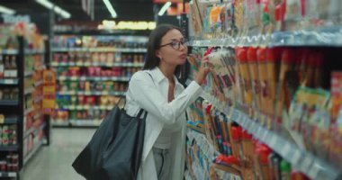 Sonsuz seçeneklerle dolu bir süpermarkette genç kadın seçimlerini modern tüketimde tartıyor. Milenyum hanımı, süpermarket tüketicilerinin karar verme mekanizmalarındaki ürünleri incelerken düşüncelere dalıyor.