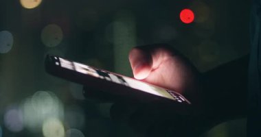 Akşamları parlayan akıllı telefonlu bir el, şehir ortamındaki gece atmosferini yakalıyor. Gece ortamı dijital bağlantıyı vurguluyor, modern pazarlama veya yaşam tarzı projeleri için mükemmel